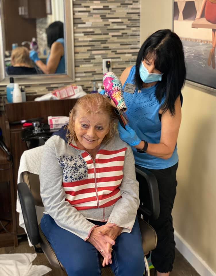 A senior citizen having her hair done with care by a staff member at an assisted living facility