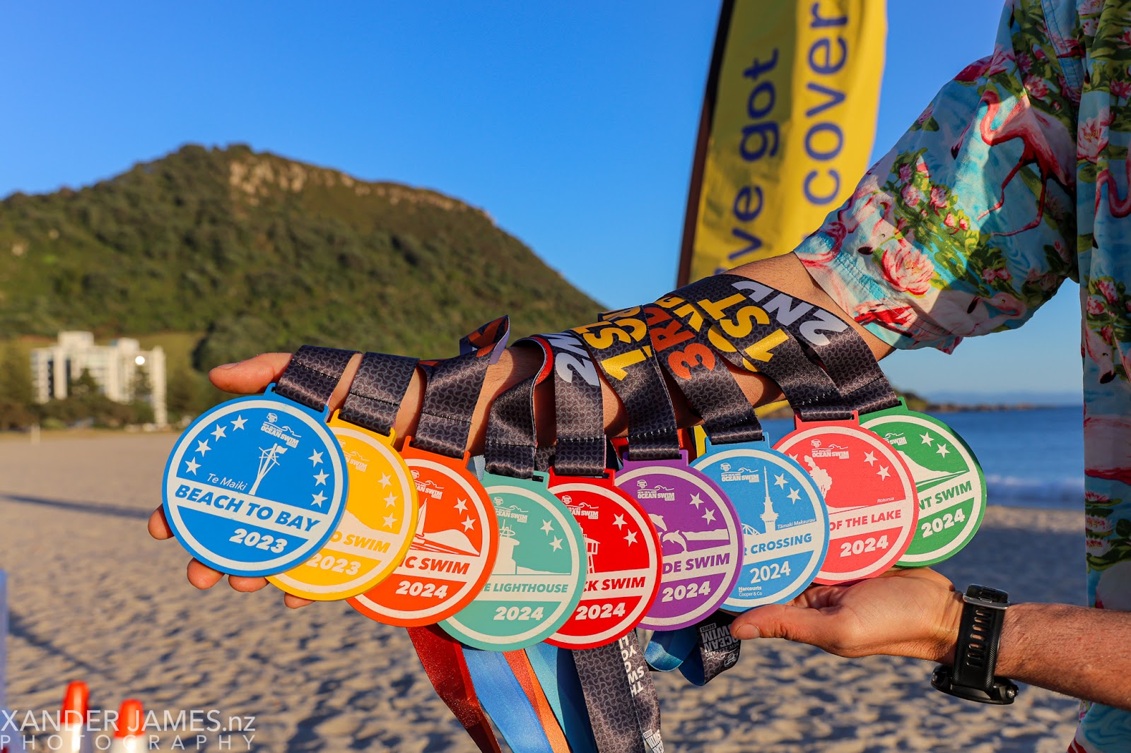Nine coloured custom wooden medals, made for the New Zealand Ocean Swim Series, in a row.