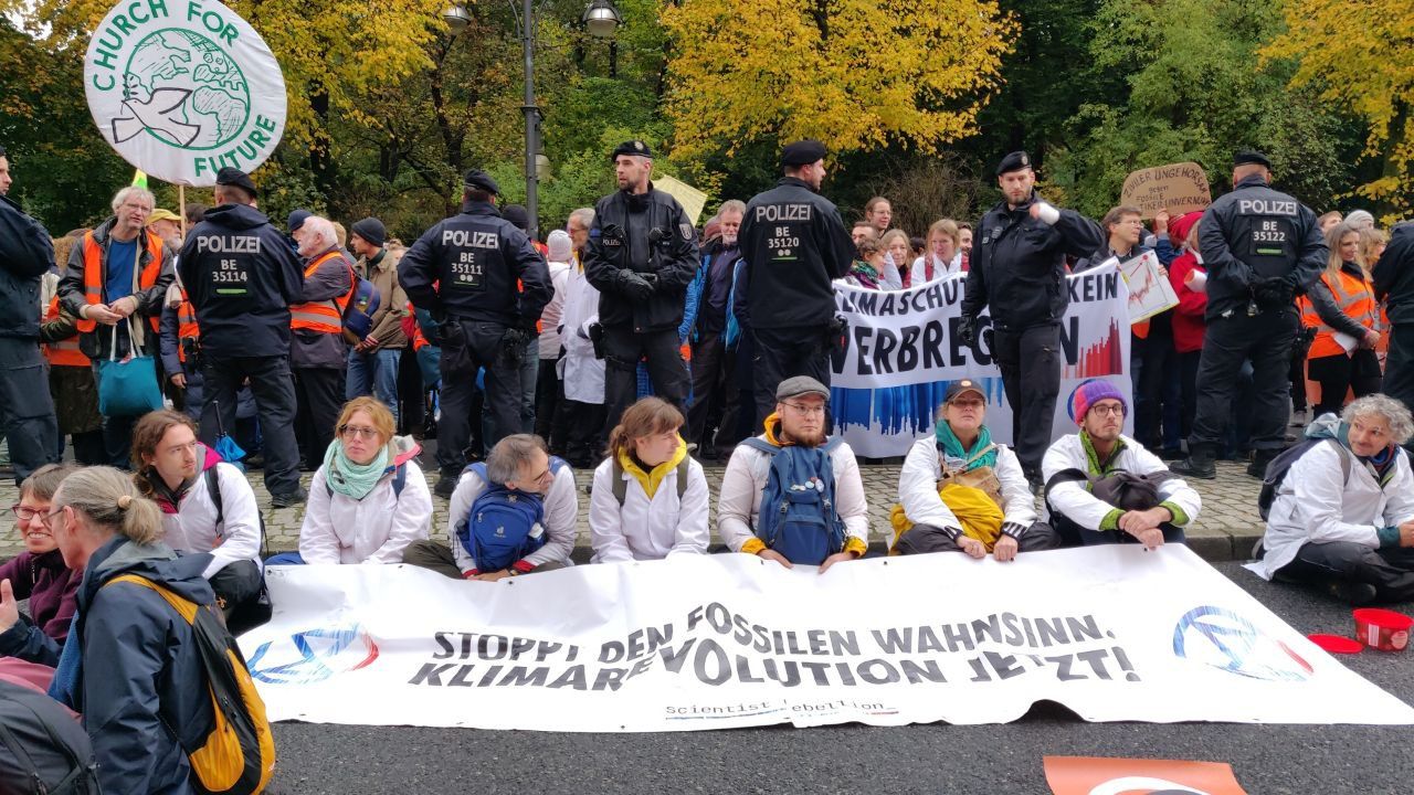 A dozen Scientist Rebellion Germany activists sit on the road in a line with a banner 