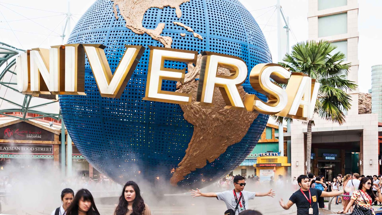 Pengunjung dengan ekspresi gembira di depan landmark ikonis Universal Studios Singapore, dengan globe besar bertuliskan 'UNIVERSAL' sebagai latar belakang.