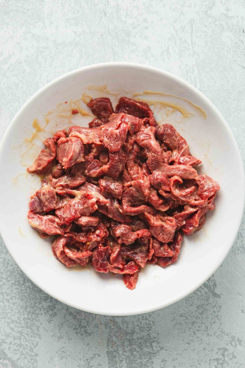 Raw beef in a white bowl on a grey background.