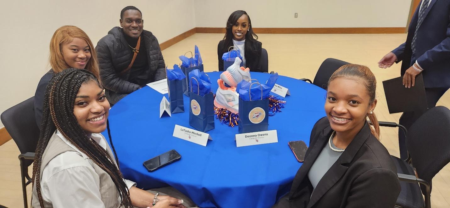 A group of people sitting around a blue table

Description automatically generated