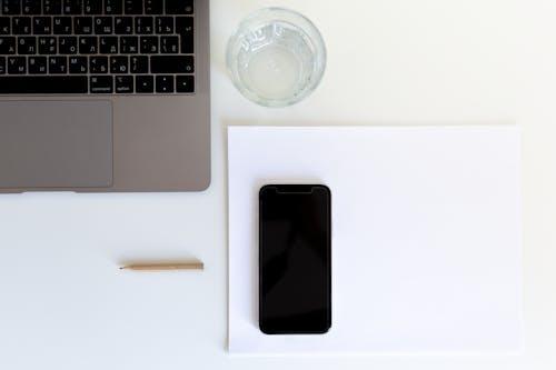 Free From above of smartphone placed on white paper with laptop and glass of water preparing for working day in modern workplace Stock Photo