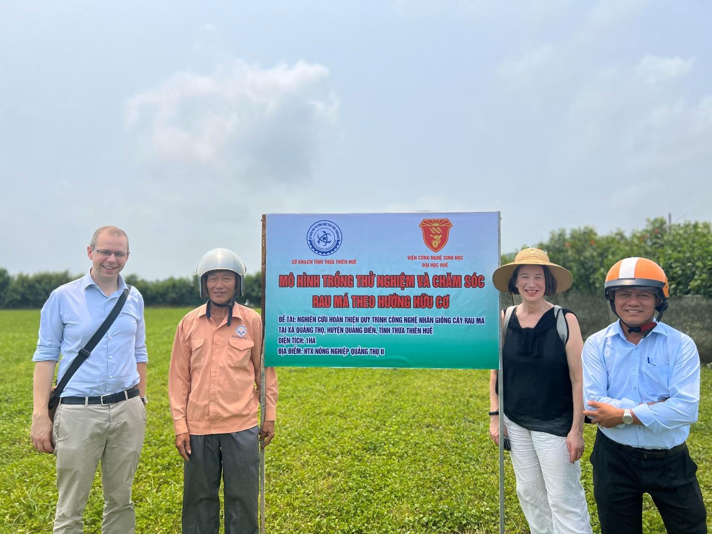 A group of people standing in a field holding a sign Description automatically generated