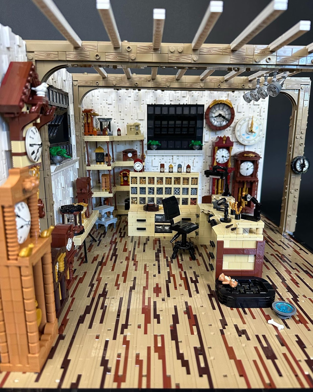A photo of the Lego Creation Clockmaker's Studio by Kelly Bartlett, showing a cozy store with clocks of many different styles lining the walls, a desk chair and desk with tools, and an organizer with clock parts
