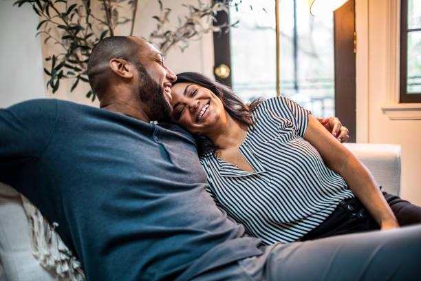 married couple embracing on sofa - black man love stock pictures, royalty-free photos & images