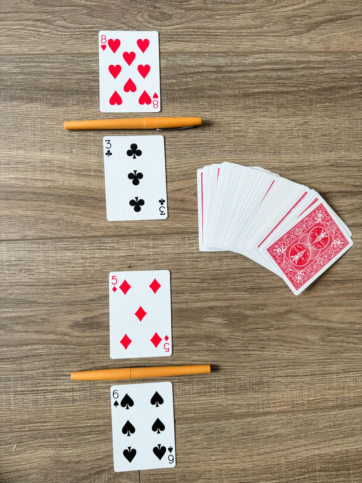 This image shows a deck of cards and four flipped over. The four flipped cards create two different fractions. Two cards are separated by a pen. The fractions are 3/8 and 5/6. 