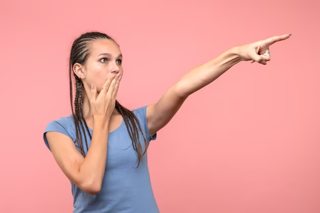 A surprised girl with one hand on her mouth and the other pointing outwards