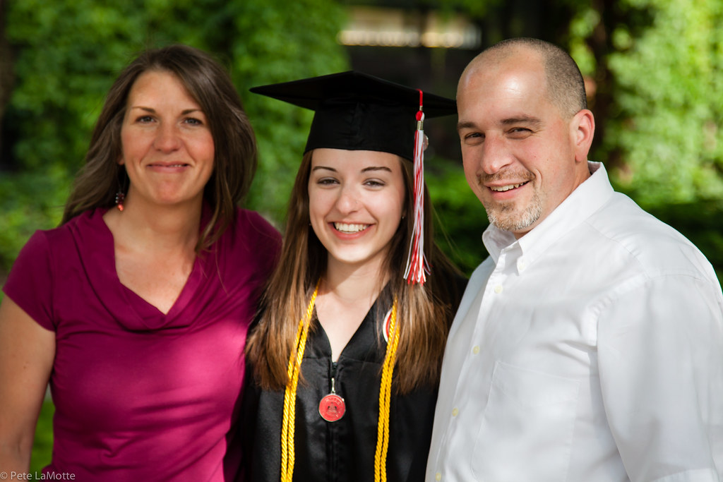 A happy student in graduation gown with her happy parents.