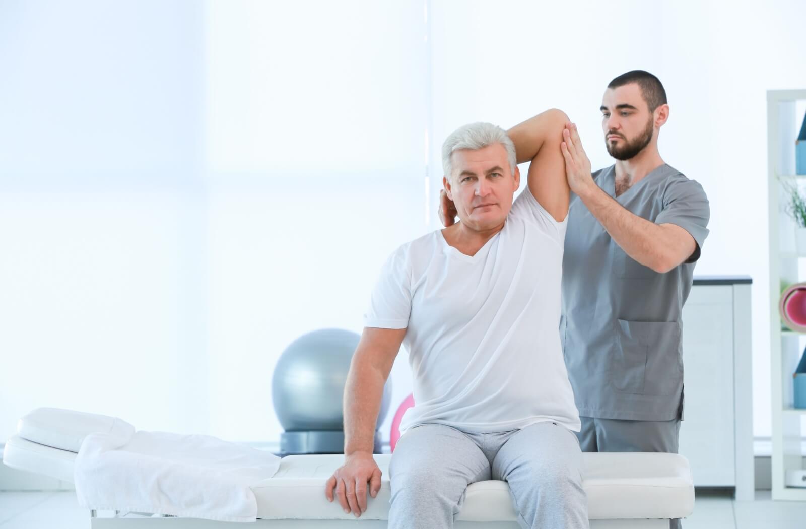 A physiotherapist assisting a senior patient with his stretches.