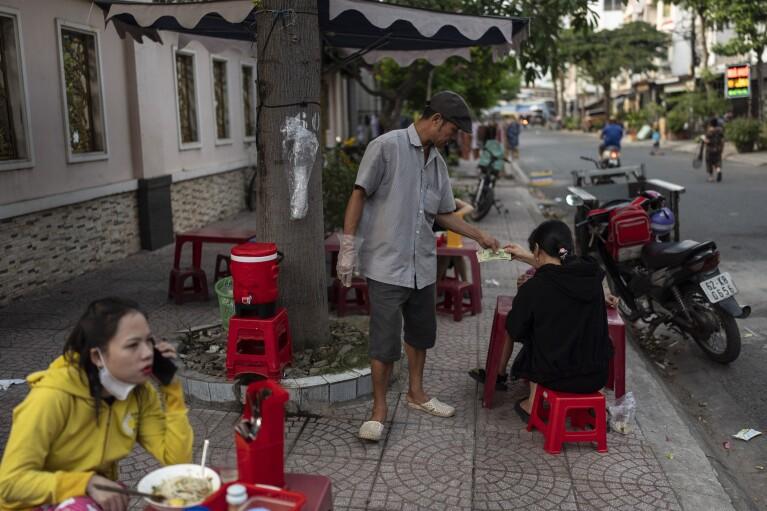 Pham Van Sang, a street food vendor who moved from the Mekong Delta, takes money from his customer in Ho Chi Minh City, Vietnam, Monday, Jan. 22, 2024. He sells noodles in the city's industrial zone, a popular destination for many migrants from the Mekong Delta seeking a better life as he did. (AP Photo/Jae C. Hong)