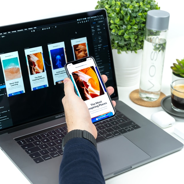 A man holding a phone with UI/UX design in front of a laptop