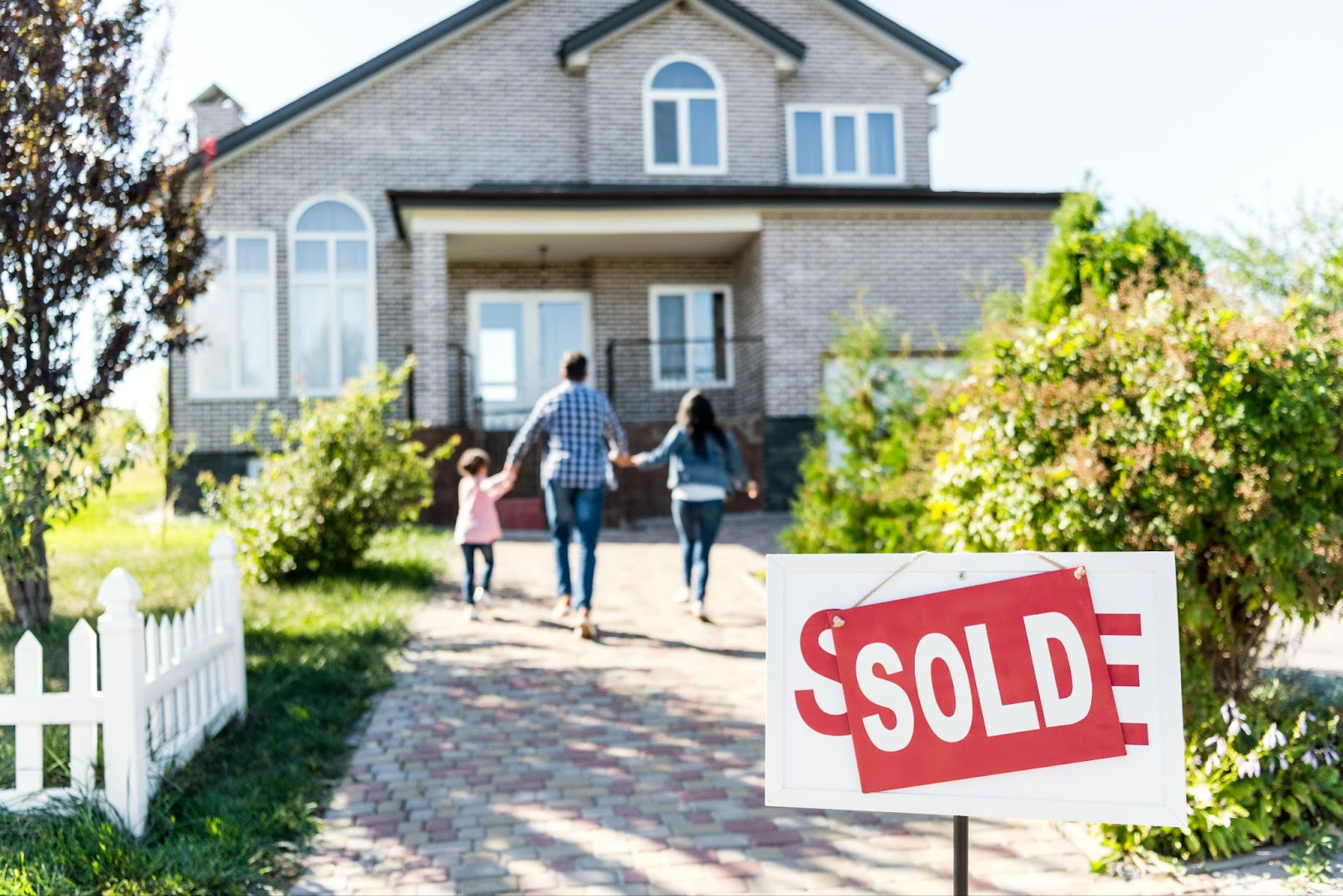 A family happily walks past a sold sign in front of their new house, symbolizing a successful purchase and a fresh start for their future.

