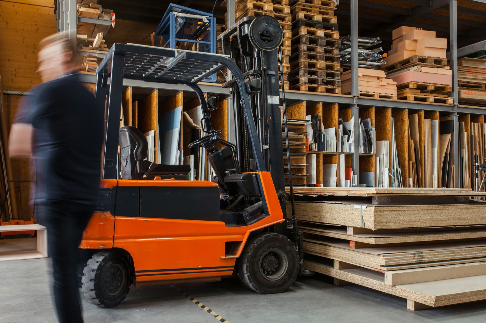 A forklift hauling wood, with a person walking by the forklift
