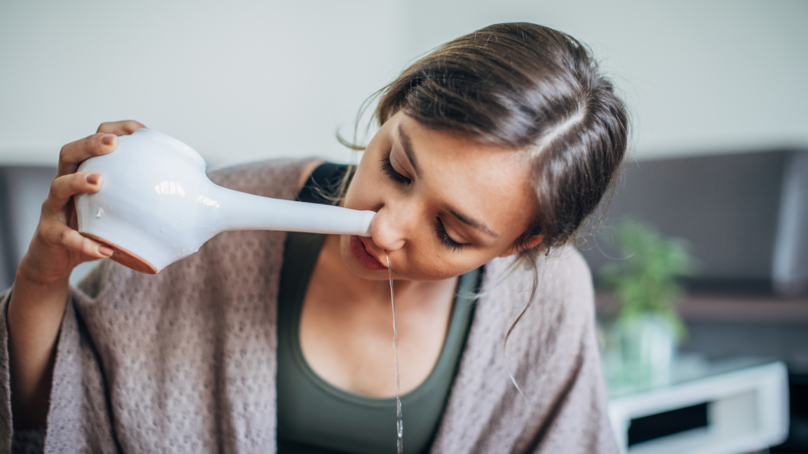  A woman rinsing her nose using a neti pot to treat allergies naturally