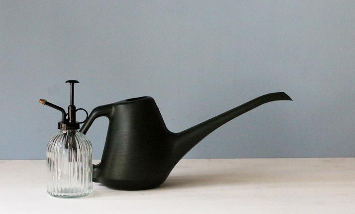 A black watering can and water spray on a wooden table