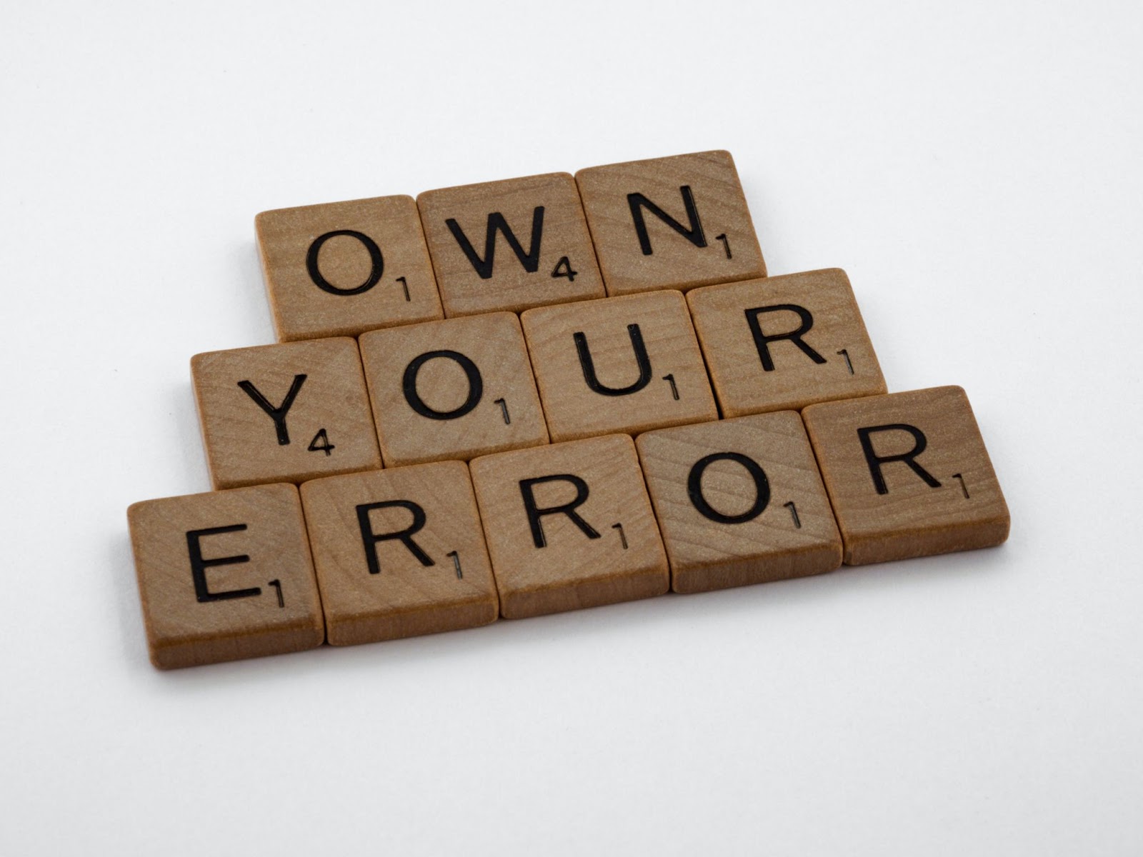 Scrabble tiles on a white background spelling out “Own your error”