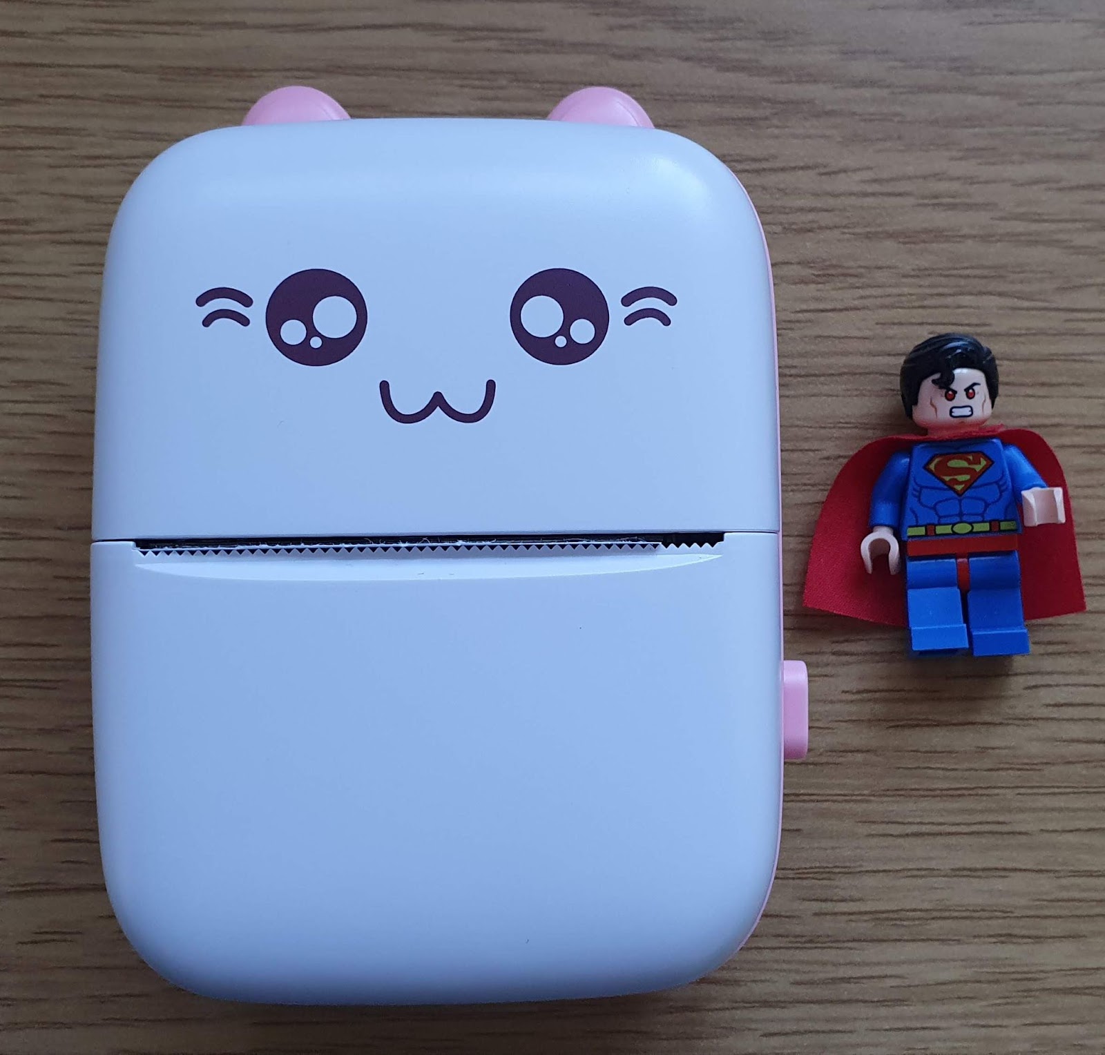 Thermal printer with a stylised cat face next to a Lego superman minifig for size comparison