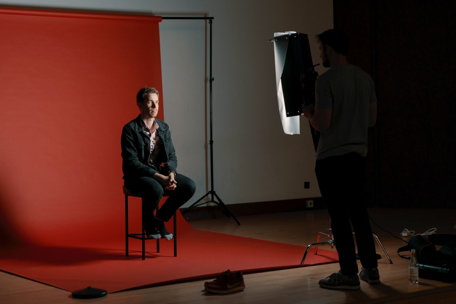 A guy sitting on a chair in a studio in front of a paper roll background poses for his professional headshots.