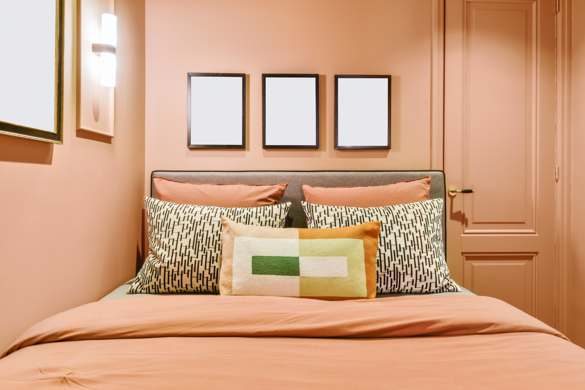 A bedroom painted in the color peach fuzz with a matching made bed and pillows with geometric prints