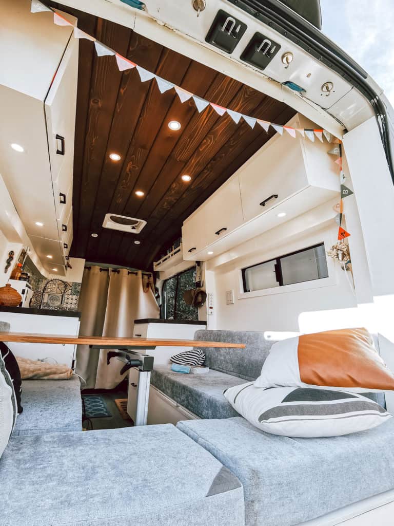 Ford Transit camper van interior showing couches, ceiling, lights, and over head cabinets.