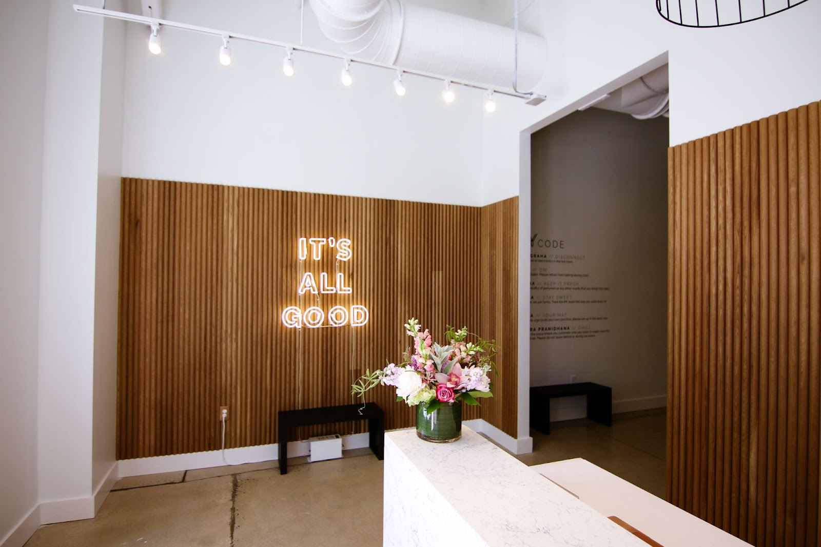 Waiting area at Midtown Yoga, a neon sign reads "It's All Good"