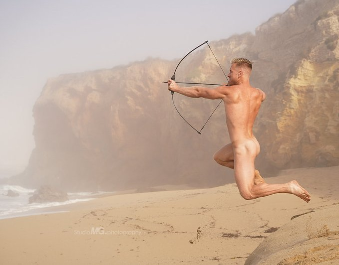 sumner blayne playing with archery doing his best katniss everdeen impression on sandy dunes in a naked gay beach photo