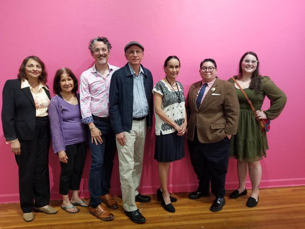 A group of people standing in front of a pink wall  Description automatically generated