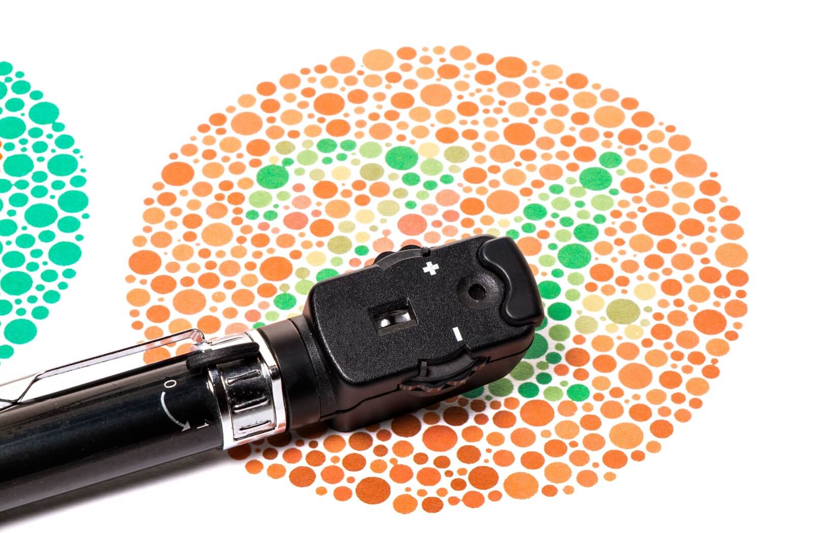 A close-up of an phthalmoscope is on a Ishihara color vision test chart.