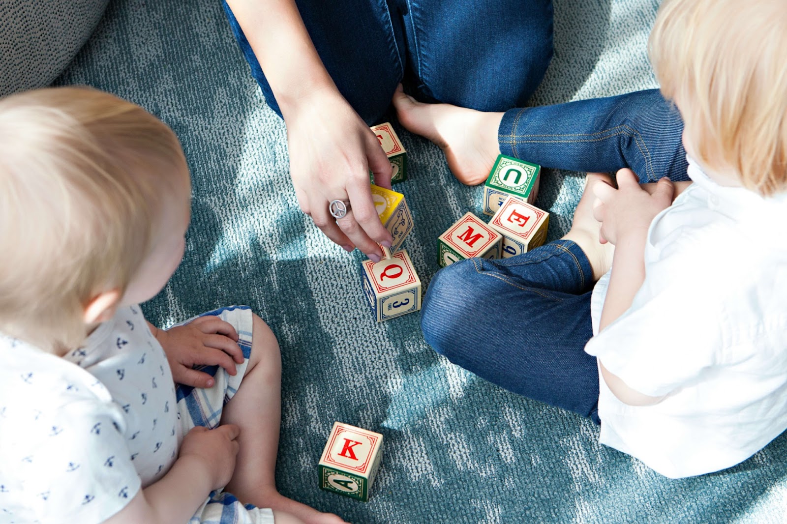 adult and two children sitting on floor playing with wooden blocks