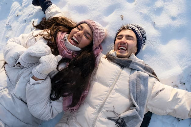 A couple joyfully laughing while lying in the snow.