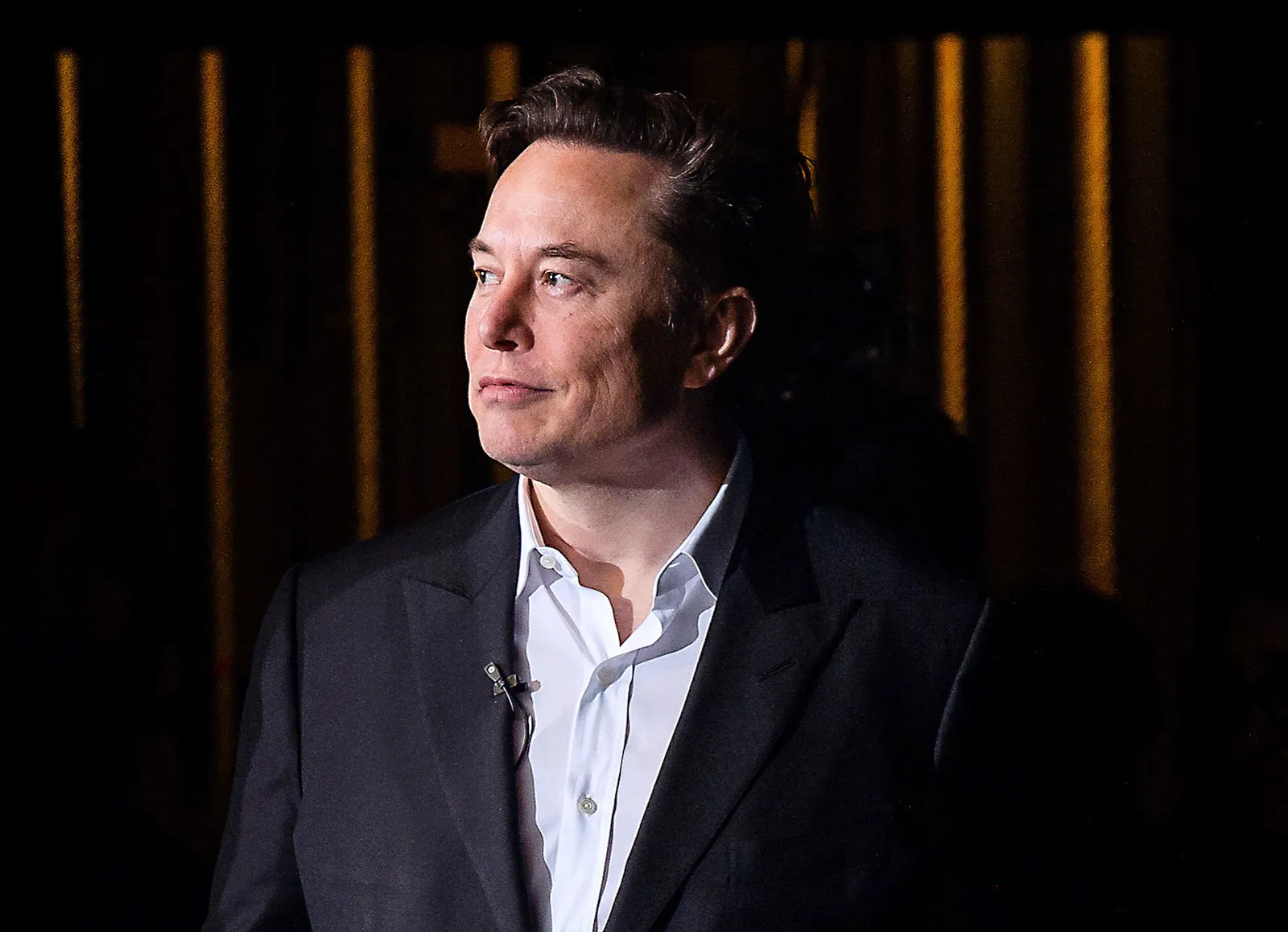 Imagem de Elon Musk de perfil, usando um terno preto com blusa social branca