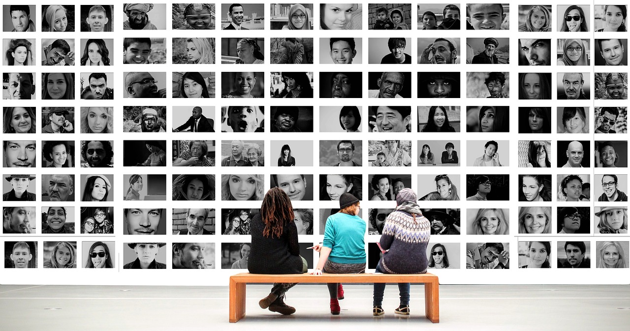 three gallery visitors sitting in front of a wall of black and white photographs of various people