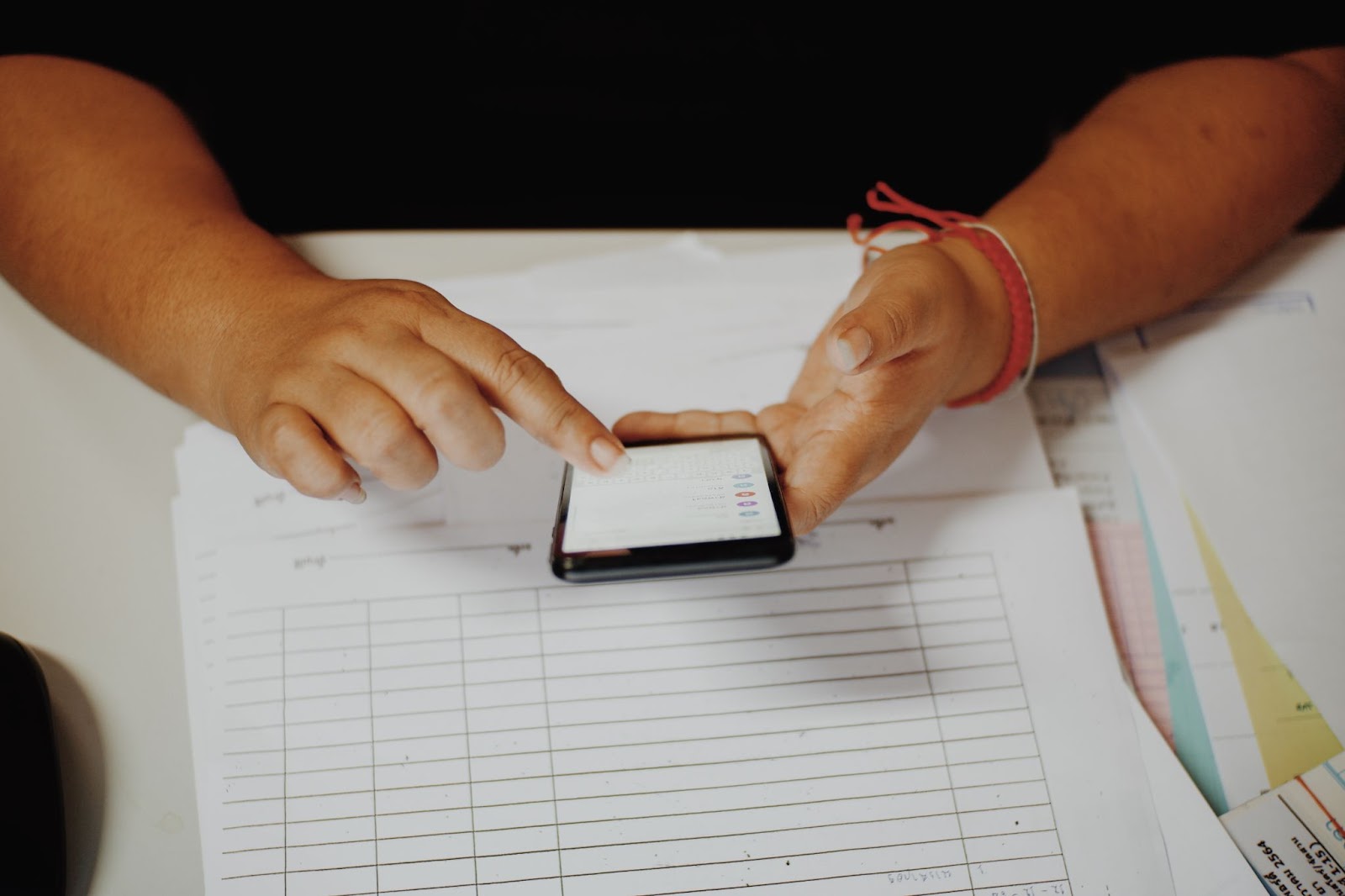 A cropped shot of a man in a black shirt using a smartphone at their workplace, focused on filling out a mobile form.