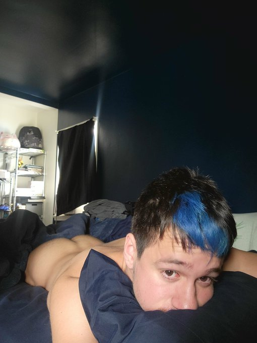 Dakota Wonders with blue hair in bed lying on his stomach and showing his tight twink ass between the covers