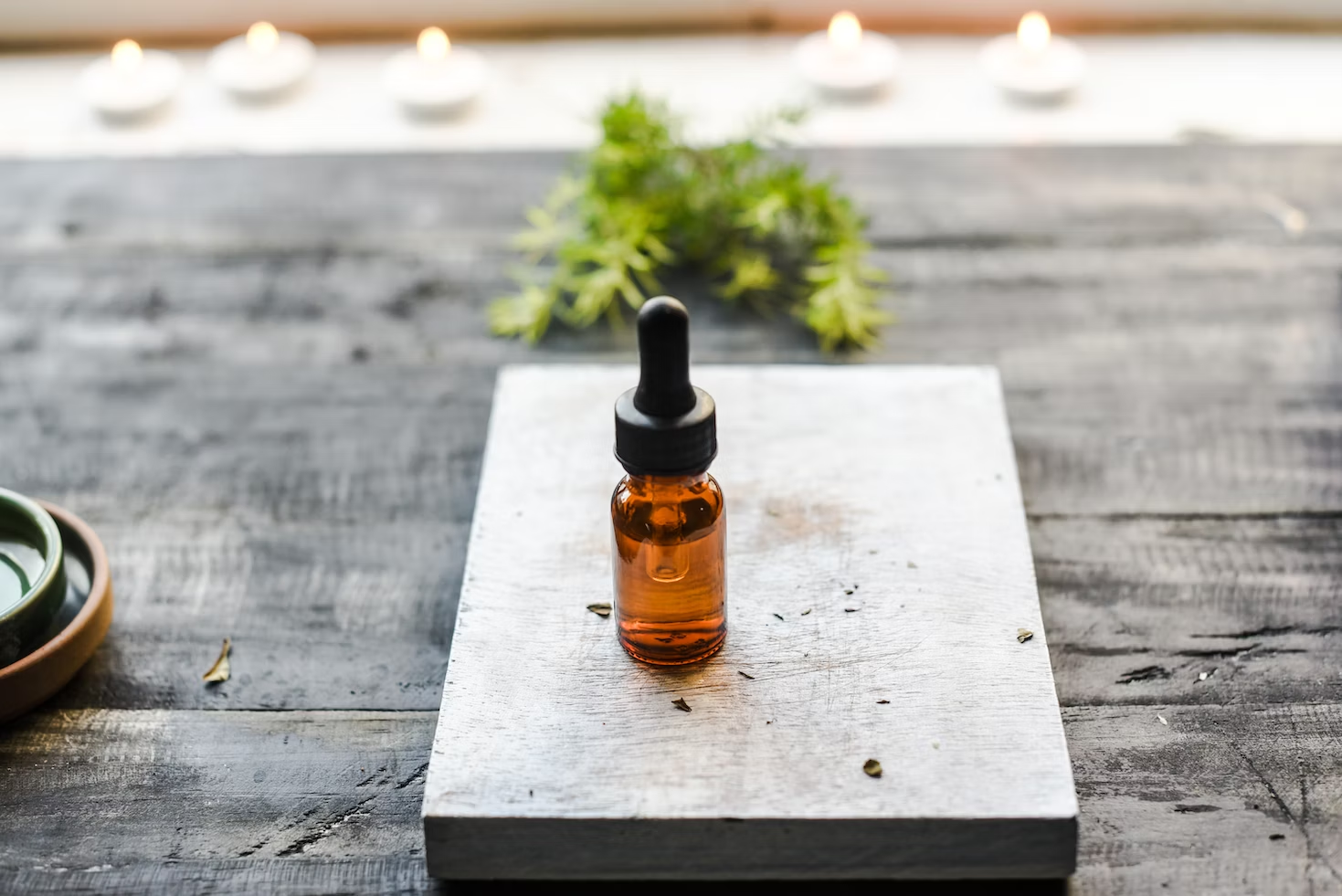 A small brown dropper bottle on a wooden block with plants in the background