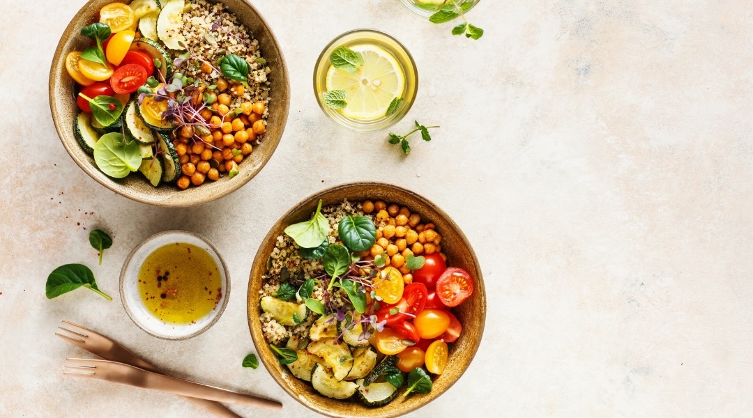 two buddha bowls with tomatoes, spinach, chickpeas, and brown rice on a beige background