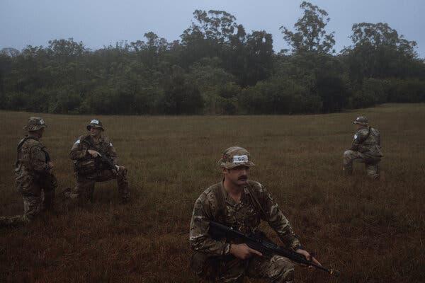 Soldiers kneel in a grassy field during a training.