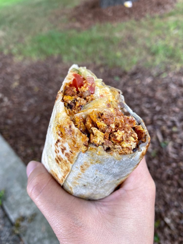 Photo from La Osita's Yelp page. A hand grips half a burrito. The burrito looks large, and it is open to show what is inside: cheese, tomato, and some kind of marinated meat.