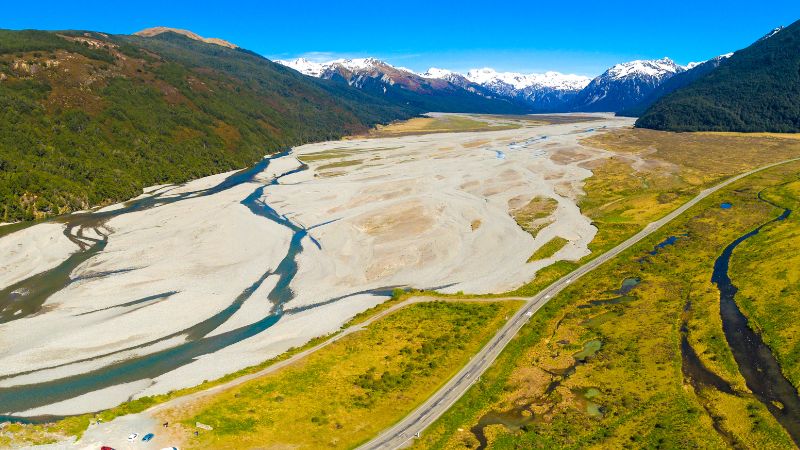 Aerial view of a winding river through a broad valley flanked by mountains in Arthur’s Pass National Park.