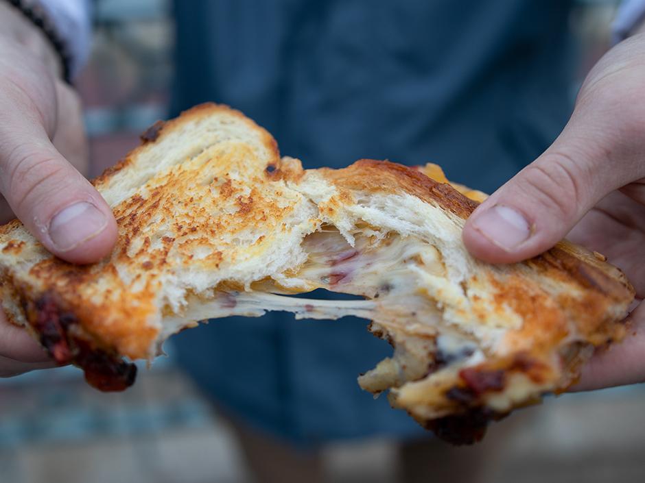 A person holding a piece the three cheese grilled cheese sandwich

