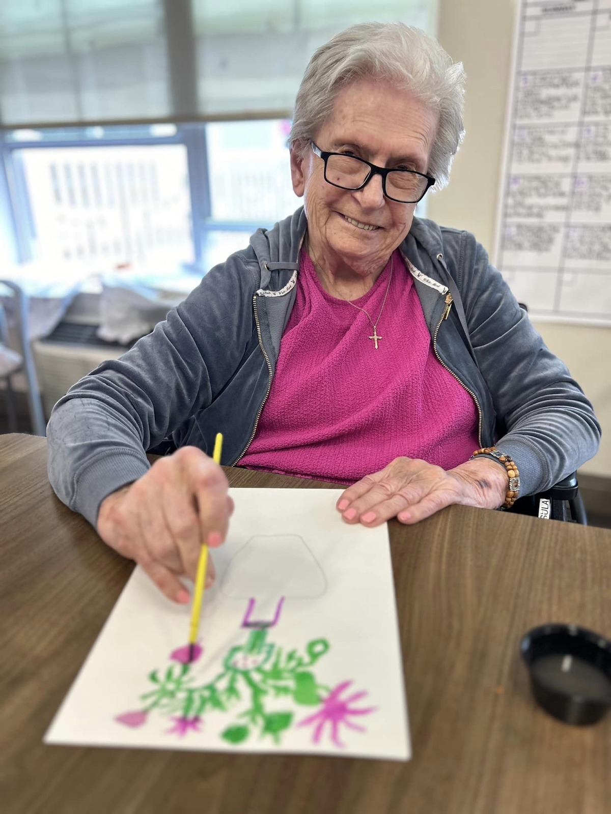 A woman with a drawing in front of her and smiling at the camera