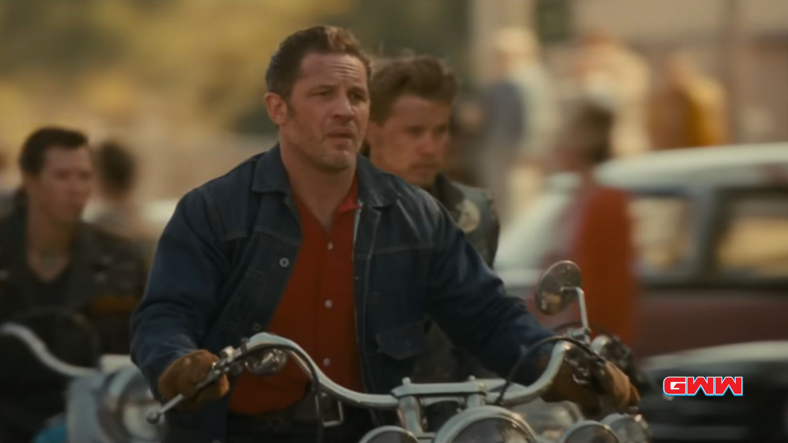 Johnny and Benny riding a motorcycle in a crowd, wearing a denim jacket.