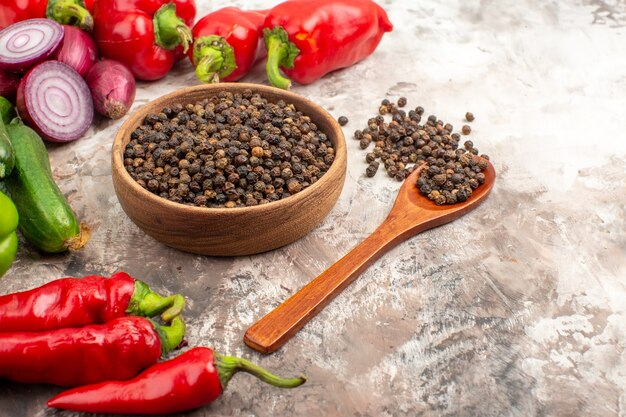 A bowl of black pepper next to red peppers and a wooden spoon  Description automatically generated