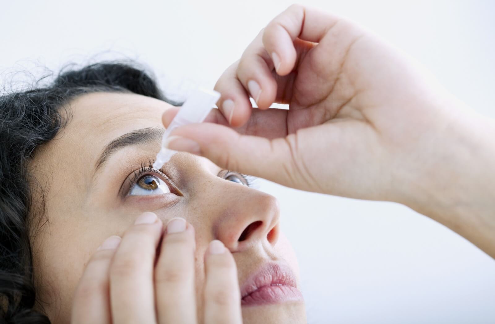A woman applying eyedrops on her right eye.