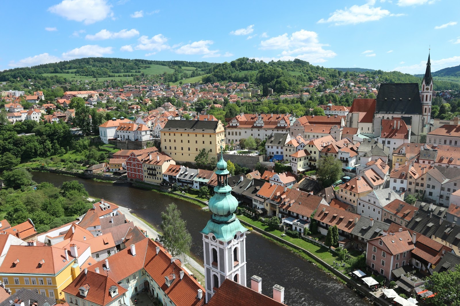 A stunning aerial view of Český Krumlov Castle perched on a hill above the Vltava River, surrounded by colorful buildings. 