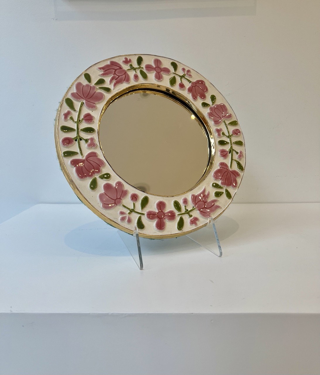A graceful floral mirror by Mithé Espelt, titled Romantic. One can observe the fine glazes of Mithé Espelt and the trace of her hand on the golden rim.