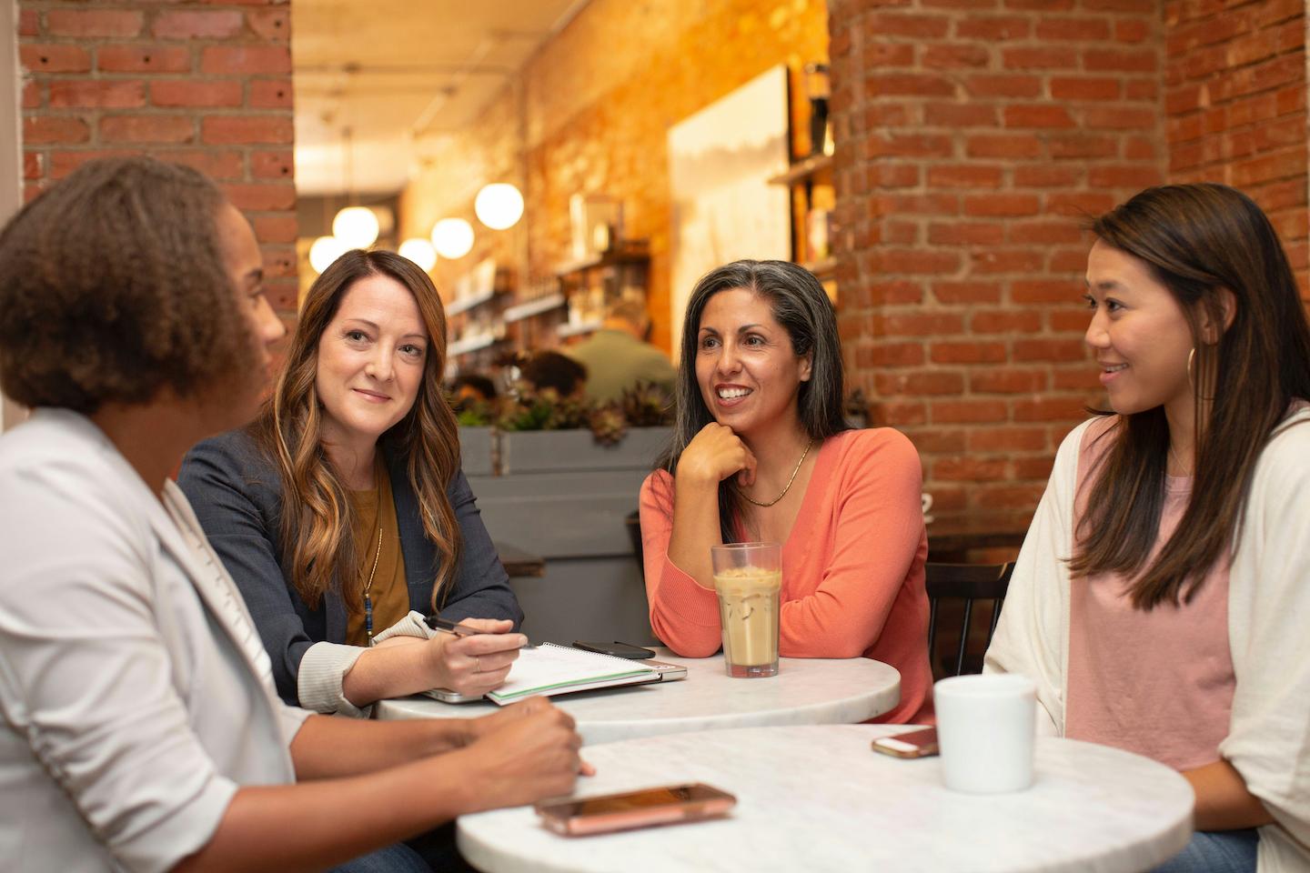 Four women seated, having coffee, talking to each other.