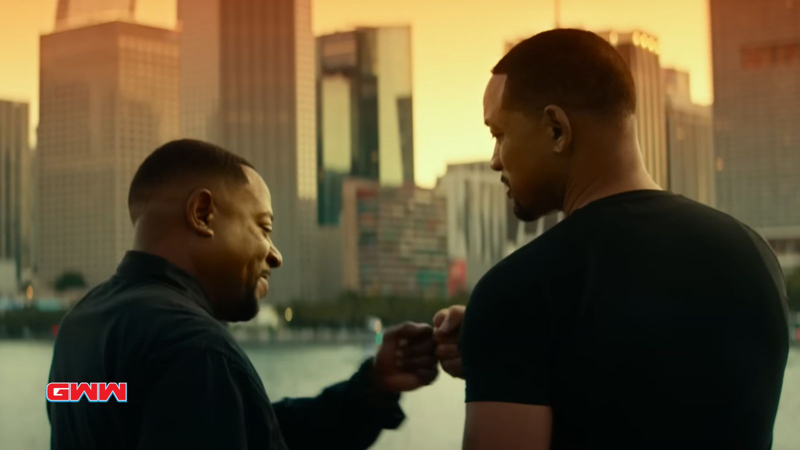 Marcus Burnet and Mike Lowrey fist-bumping with a city skyline at sunset.