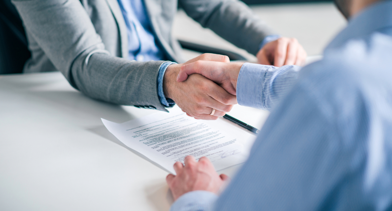 Dwie osoby podające sobie dłonie nad dokumentem, który może reprezentować umowę leasingu lub inną formę formalnej umowy biznesowej.